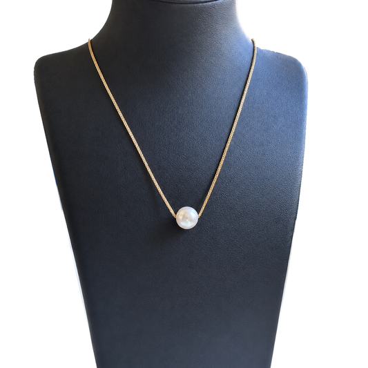 YUKI Flow necklace with a gold-tone chain threaded through a single white freshwater pearl, displayed on a black jewelry bust.