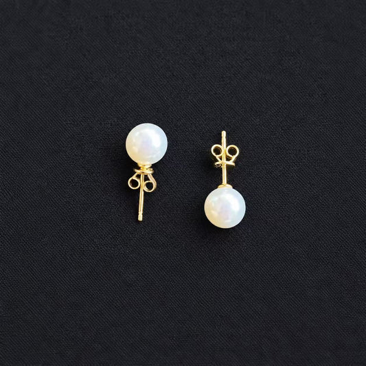 Pair of white freshwater pearl stud earrings showing gold-tone posts and butterfly backs, displayed on a black fabric background.