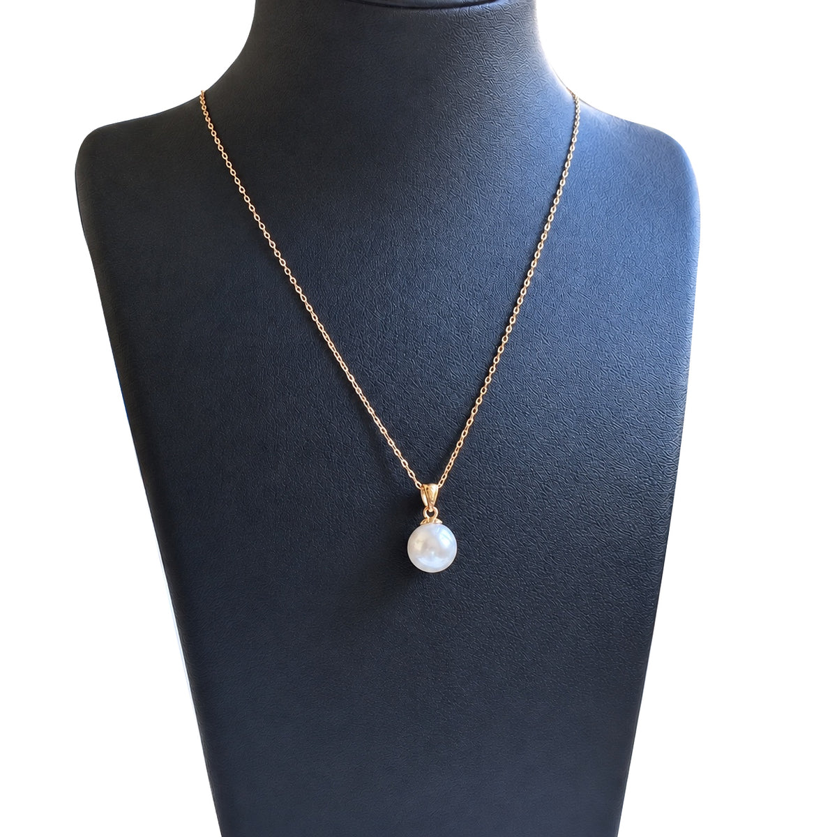 Gold-tone chain necklace with a single white pearl pendant displayed on a dark jewelry bust.