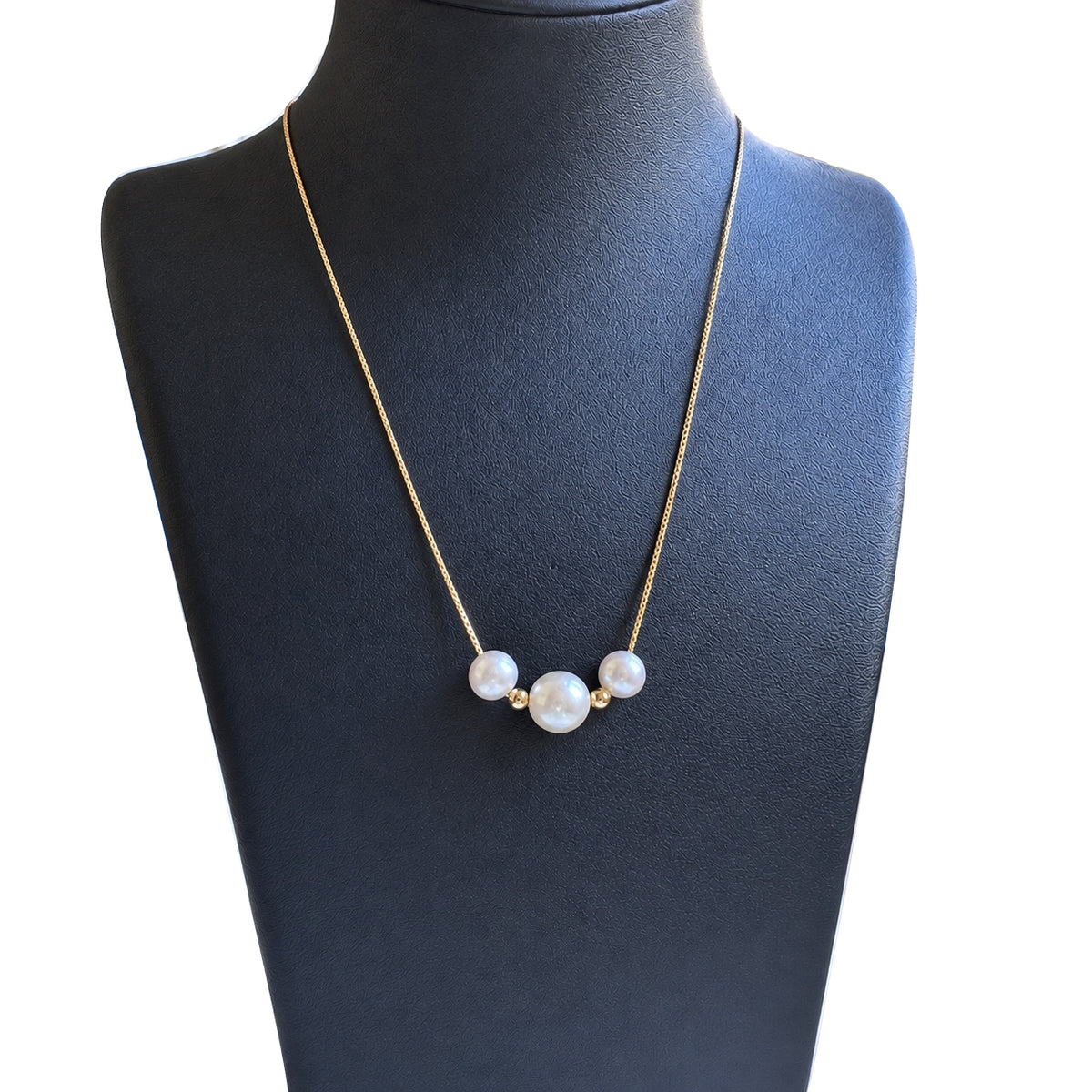 YUKI Trio necklace with three white freshwater pearls, a larger center pearl and two small gold-tone spacers, displayed on a black jewelry bust.